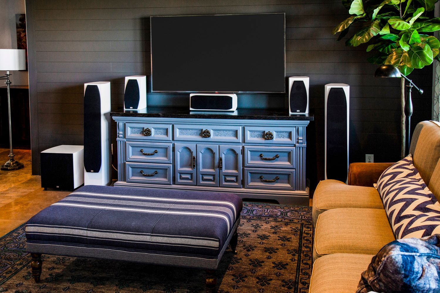 Living room with a large TV, speakers, blue cabinet, and patterned ottoman.