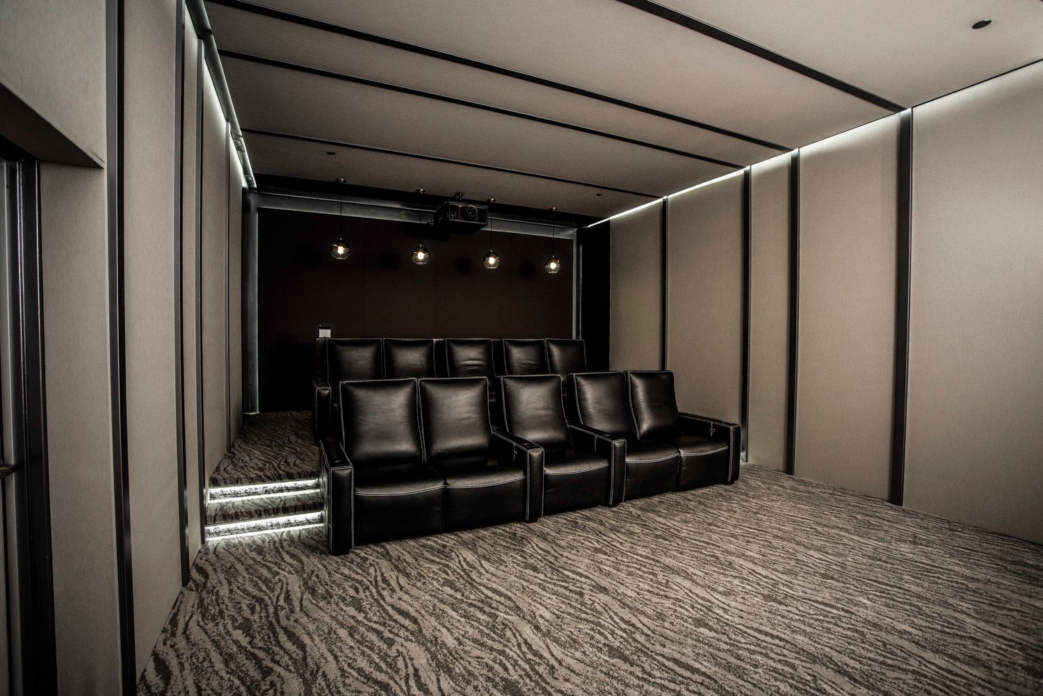 Home theater room with black leather recliners on a carpeted floor, accented by ambient lighting.