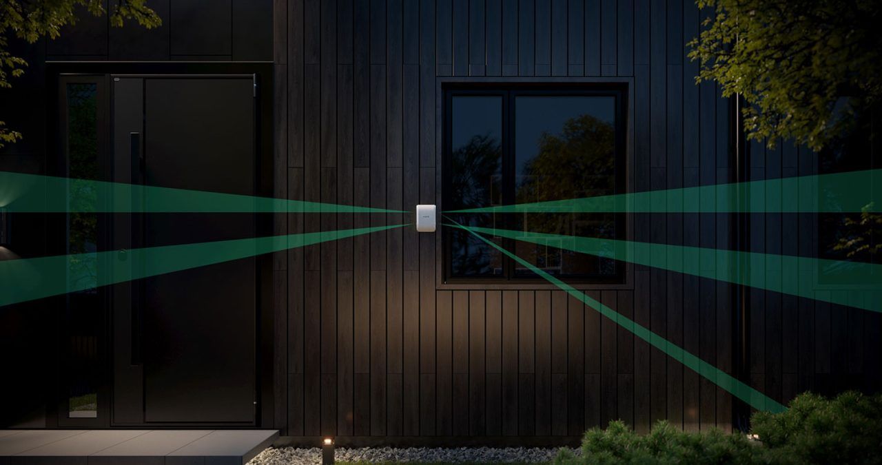 White security camera on a dark house exterior emits green laser-like beams across the yard at night.