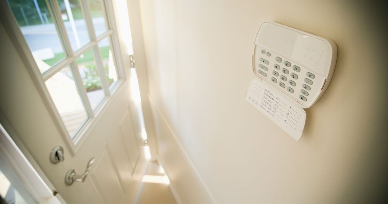 White security system keypad on a wall next to a partially open white door.