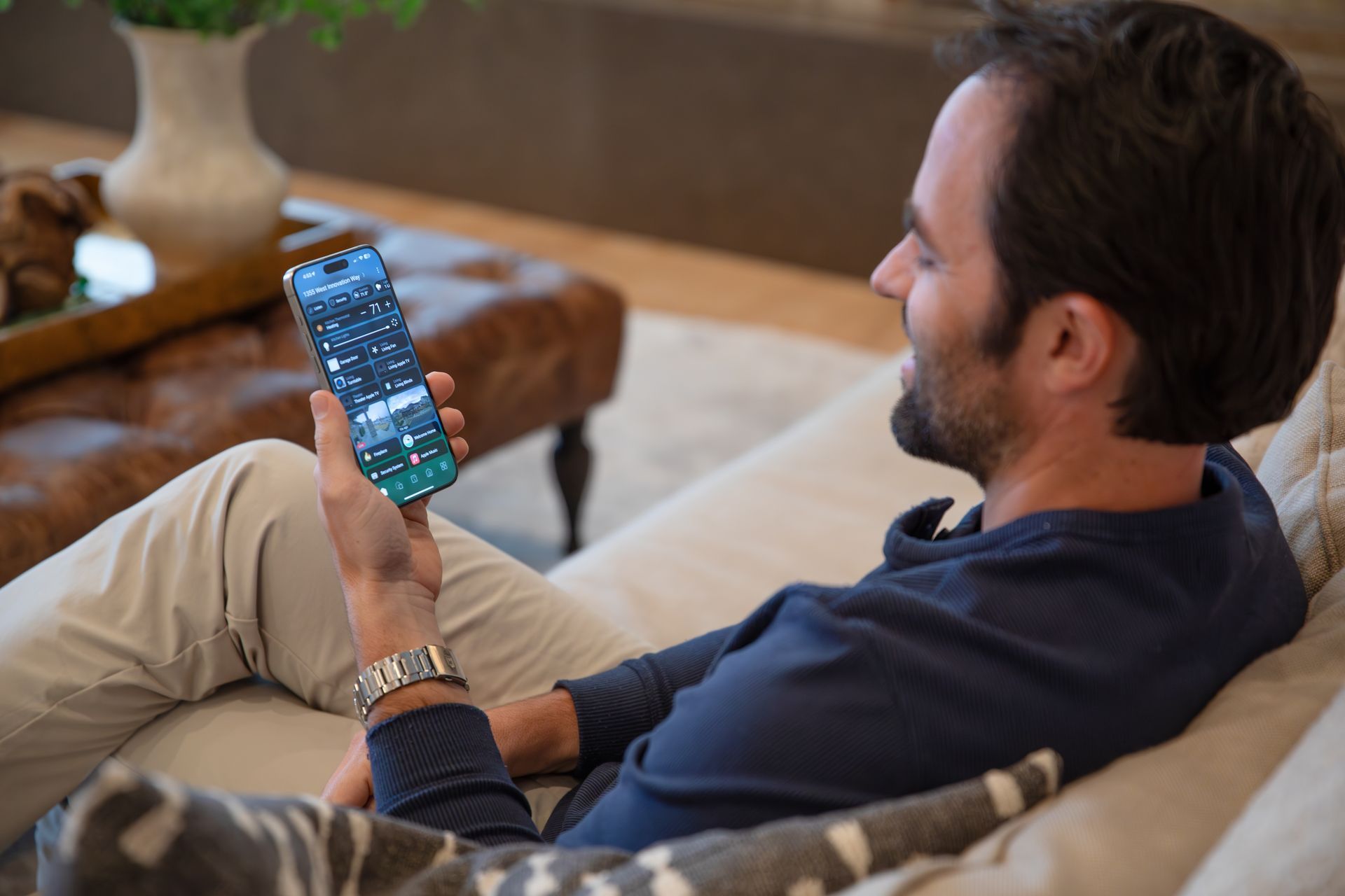 Man using smartphone to control a Control4 smart home security system, monitoring cameras and automation features from a comfortable living room in Gig Harbor, WA.