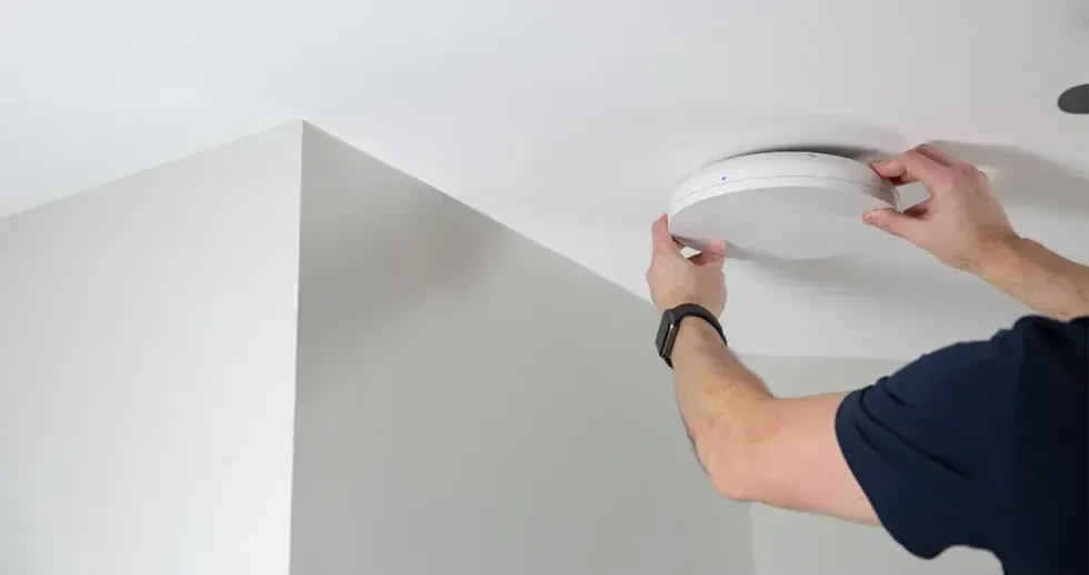 A person installing a white, round light fixture on a white ceiling.