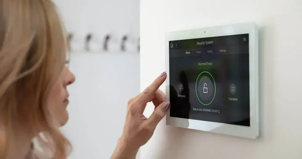 Woman using a smart home control panel to disarm a security system on a white wall.