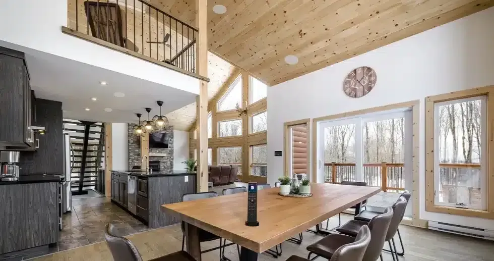 Spacious cabin interior with wooden features, dining table, chairs, and loft, plus a remote on the table.