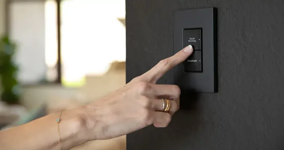 Hand pressing a black light switch on a dark gray wall.