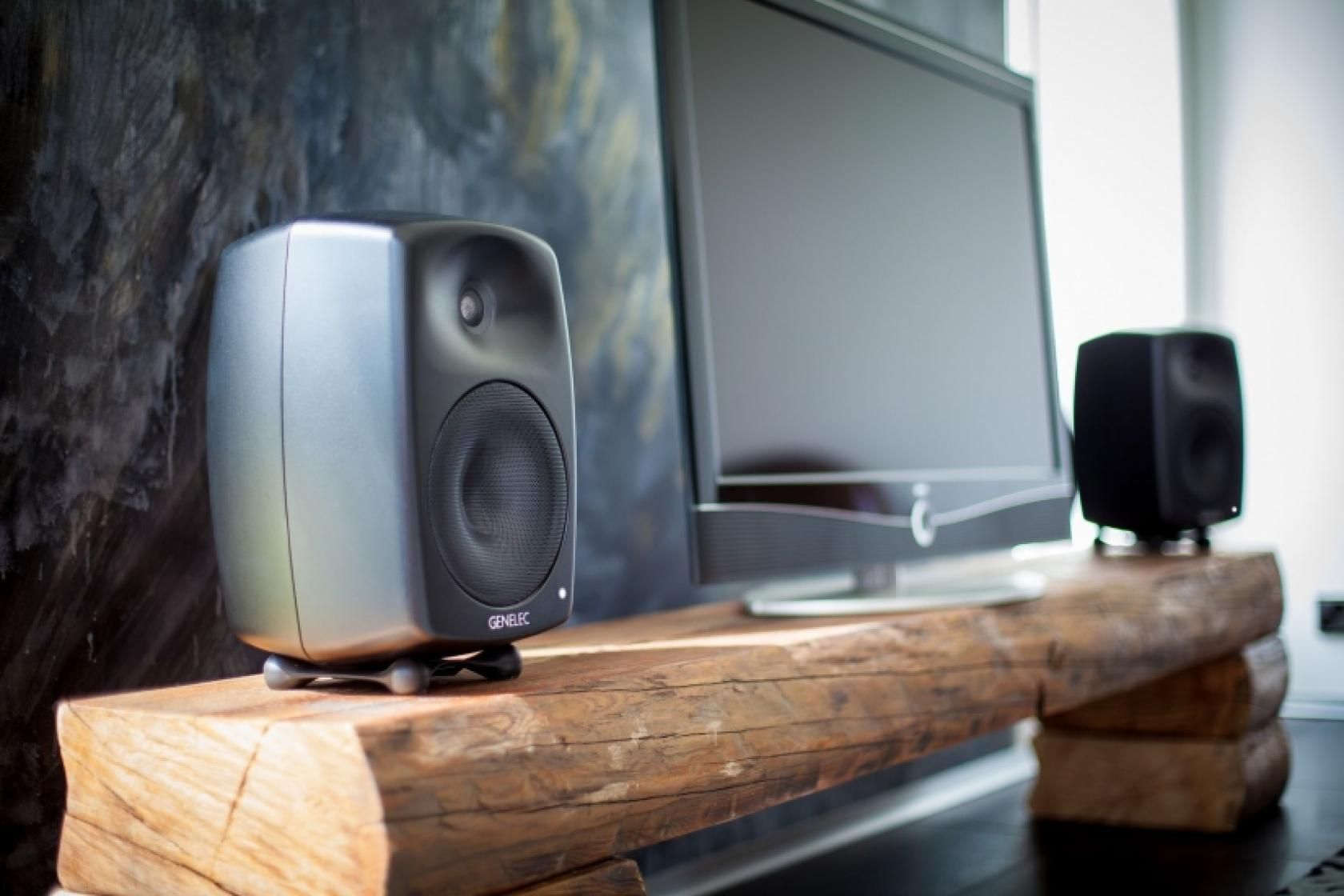 Two speakers flank a TV on a rustic wooden stand against a textured wall.