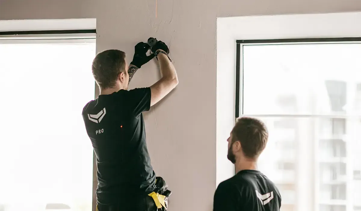 Two professional installers mounting a security or automation device on an interior wall.