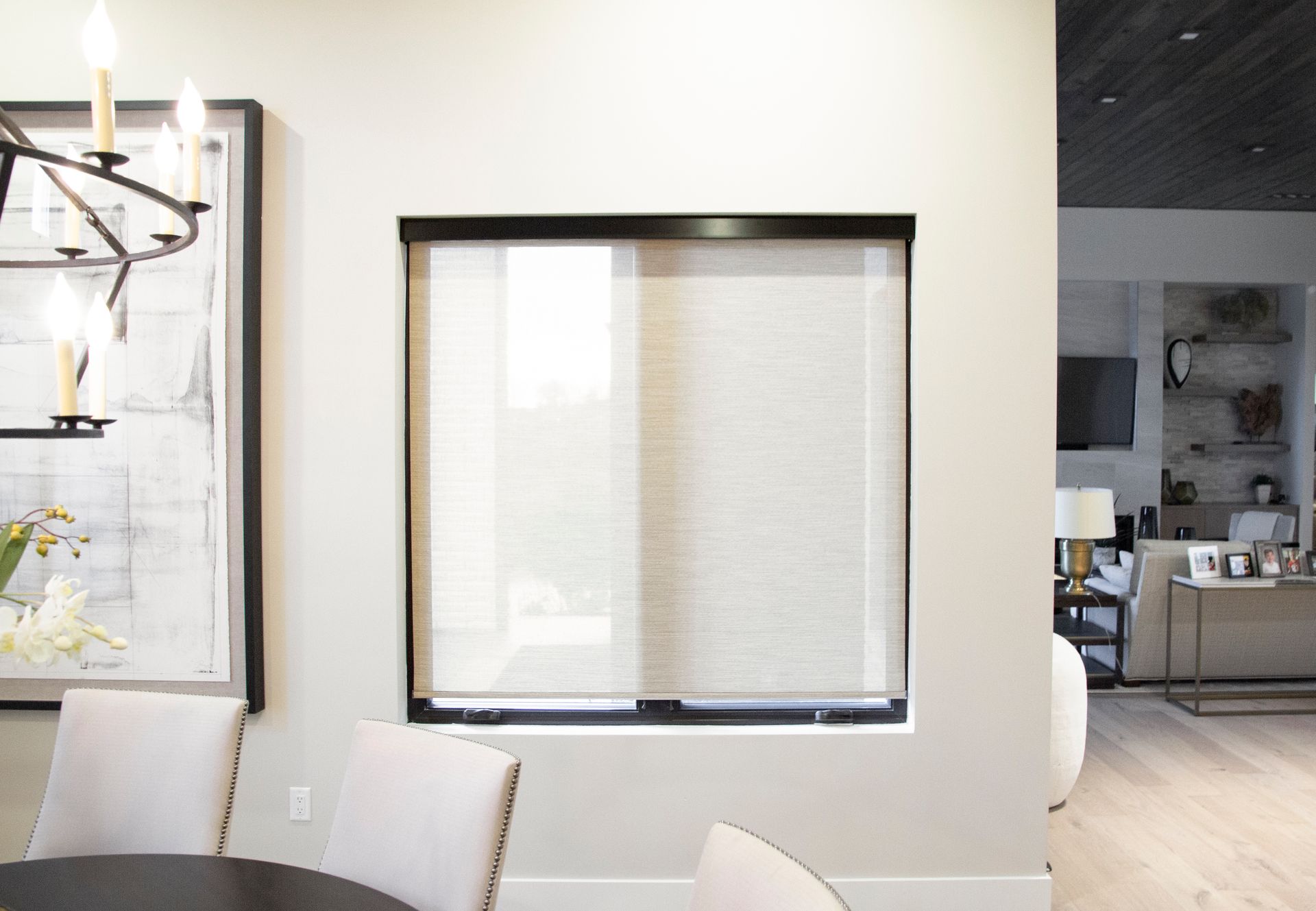 Window with light-colored roller shade, framed by a dark rectangle, inside a room with light gray walls.