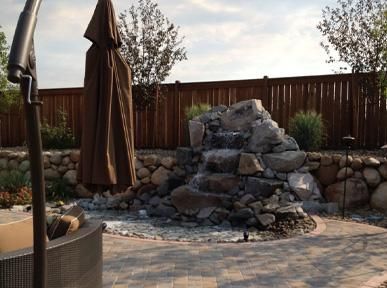 A patio with a waterfall and umbrellas in front of a wooden fence.