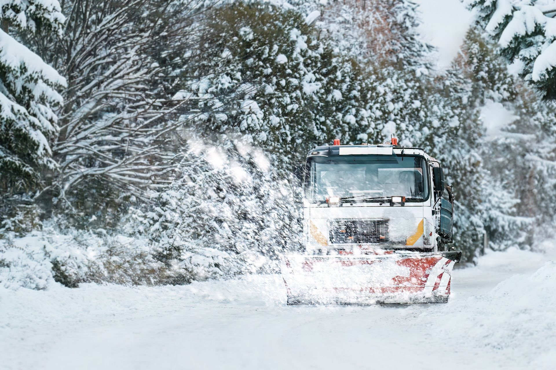 A snow plow is driving down a snow covered road.