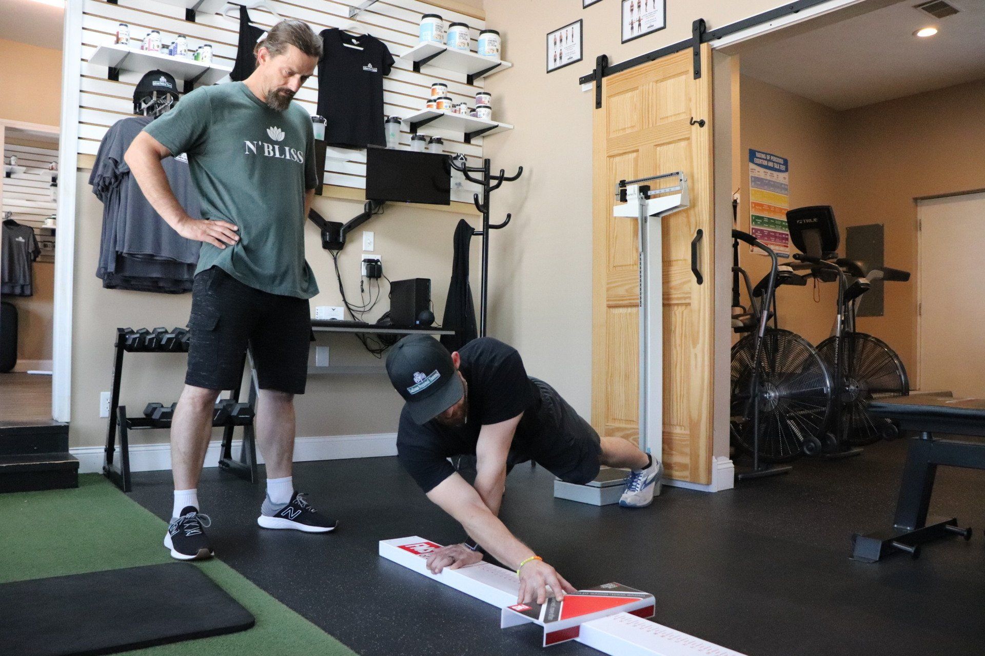 Two men in a gym, one standing and one crouching to set up a red-and-white board game.