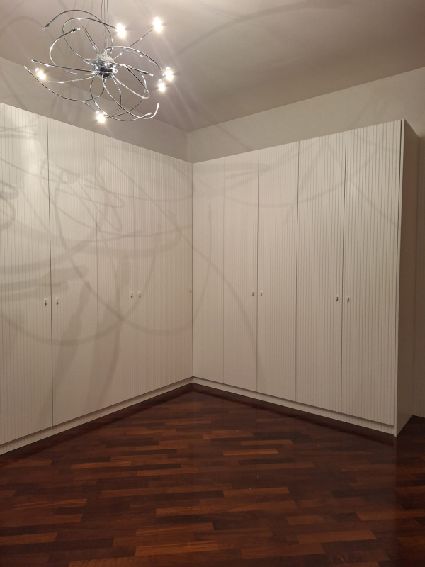 Vista d'angolo di una stanza con armadi a muro bianchi a tutta altezza, pavimento in legno scuro e lampadario moderno.