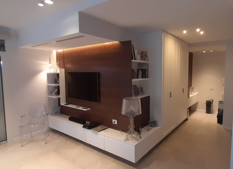 Un soggiorno moderno con televisore montato su una parete rivestita in legno, un mobile porta TV sospeso di colore bianco e un corridoio adiacente.