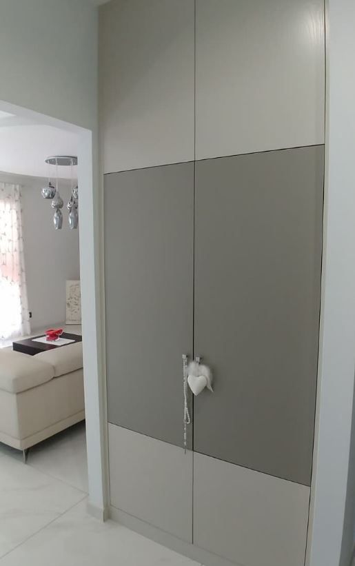 Un armadio alto a due ante con un design a blocchi di colore grigio chiaro e scuro, caratterizzato da un ornamento a forma di cuore bianco sulla maniglia.