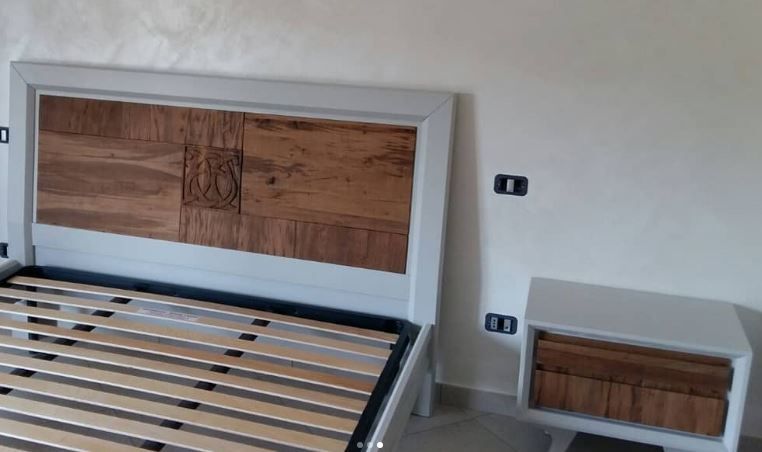 Un letto moderno con testiera in legno e comodino abbinato, su uno sfondo bianco.