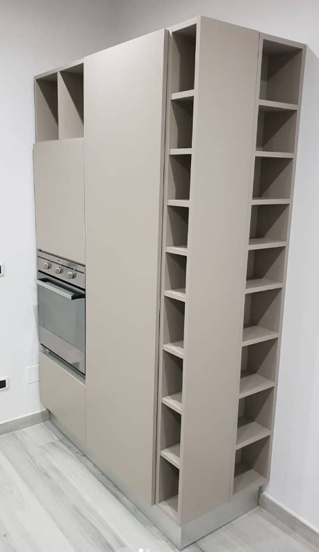 Un mobile da cucina alto, di colore beige chiaro, con forno a incasso e ripiani a giorno laterali, poggiato su un pavimento in legno chiaro.