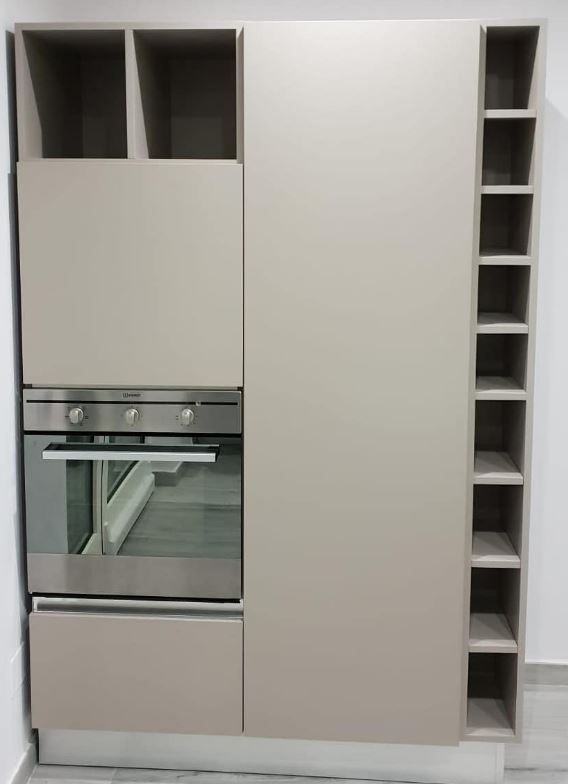 Un mobile da cucina color tortora chiaro con forno a incasso, vani portaoggetti superiori e inferiori e una scaffalatura verticale con ripiani stretti.