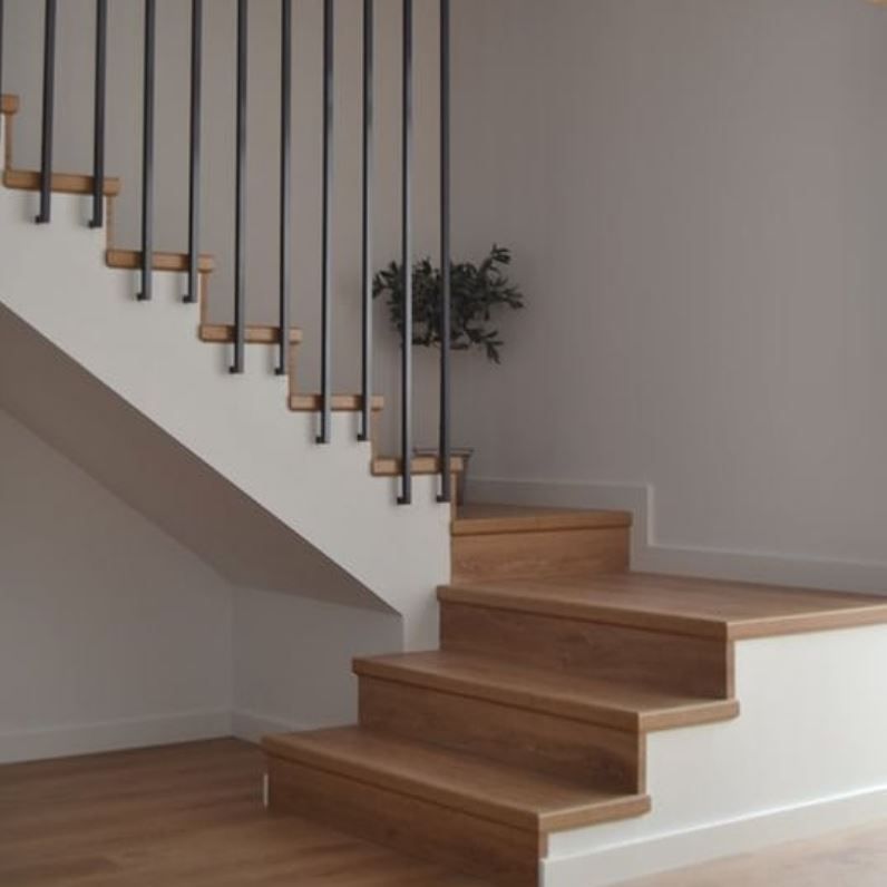 Scala moderna con gradini in legno chiaro, alzate bianche e ringhiere verticali in metallo nero su una parete bianca.