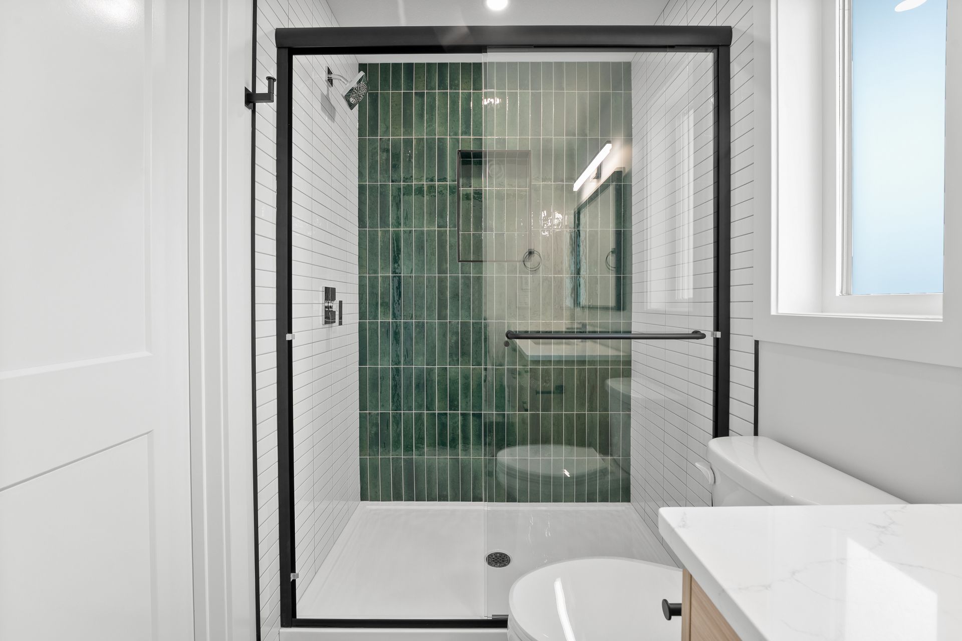Modern shower with green tile wall and glass door in white bathroom.