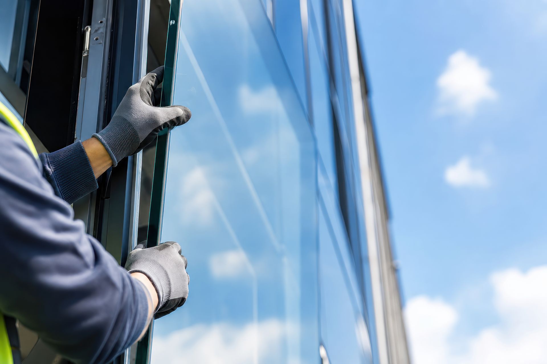 Close-up of gloved hands fitting a glass pane into a commercial glass installation on a sunny wall.