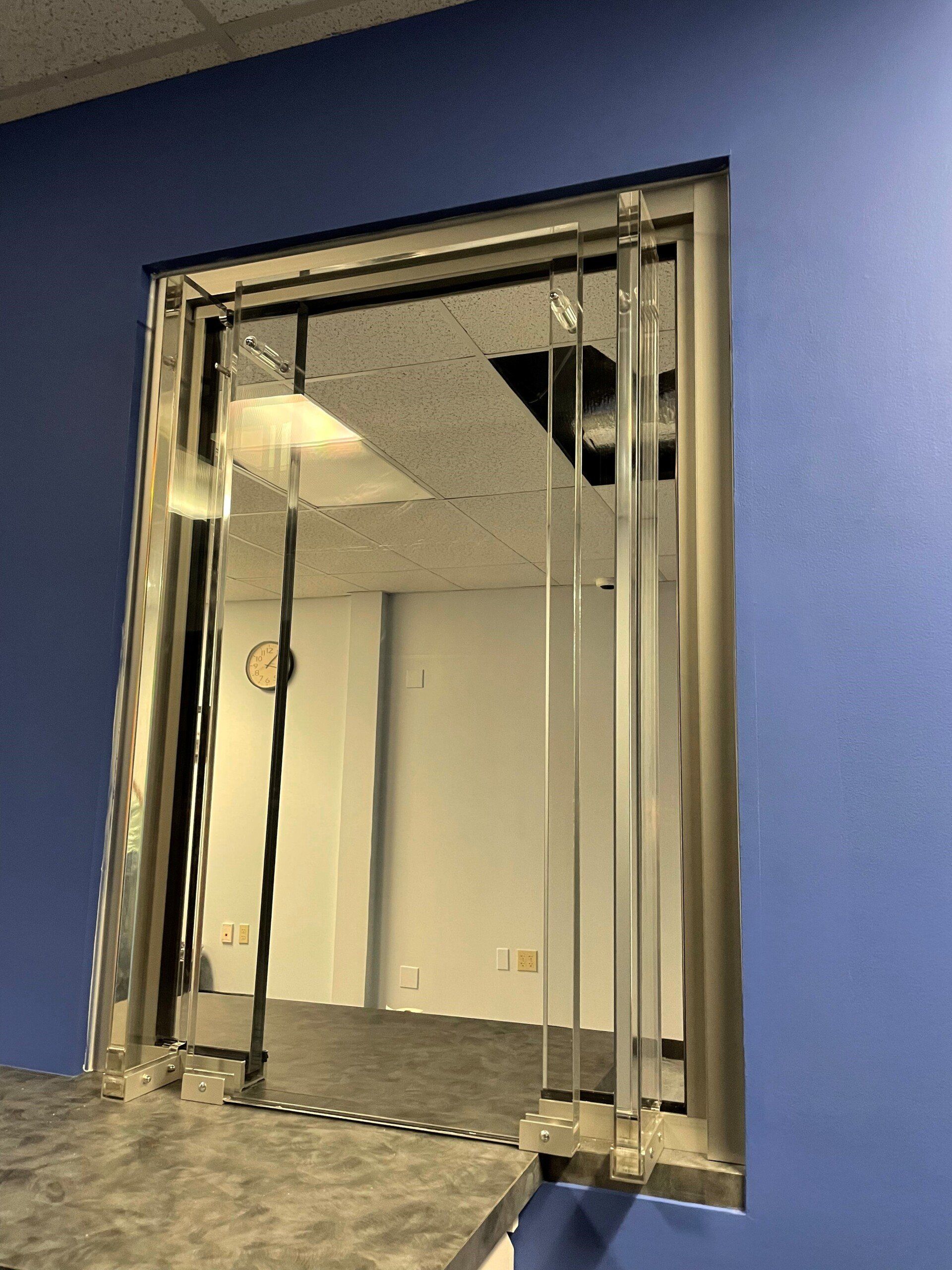 A service window with a clear acrylic barrier set into a wall painted blue.
