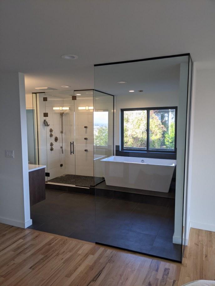 A modern bathroom with a glass-enclosed walk-in shower and a freestanding white bathtub, viewed from a wooden-floored room.