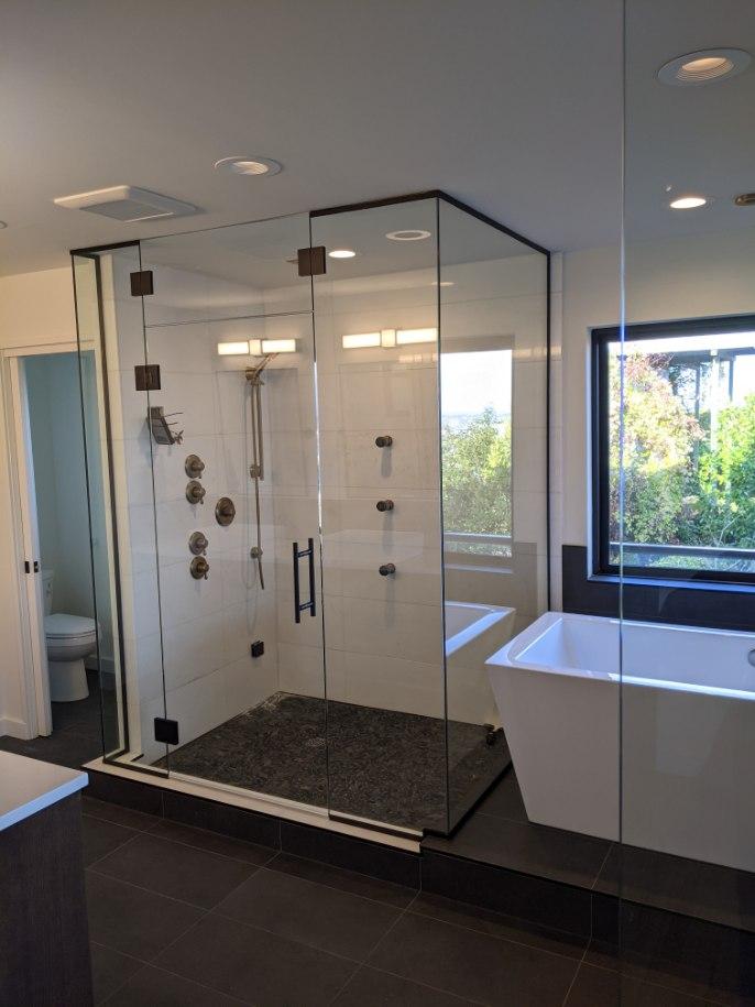Modern bathroom with a glass-enclosed shower featuring dark pebble flooring next to a freestanding white bathtub.