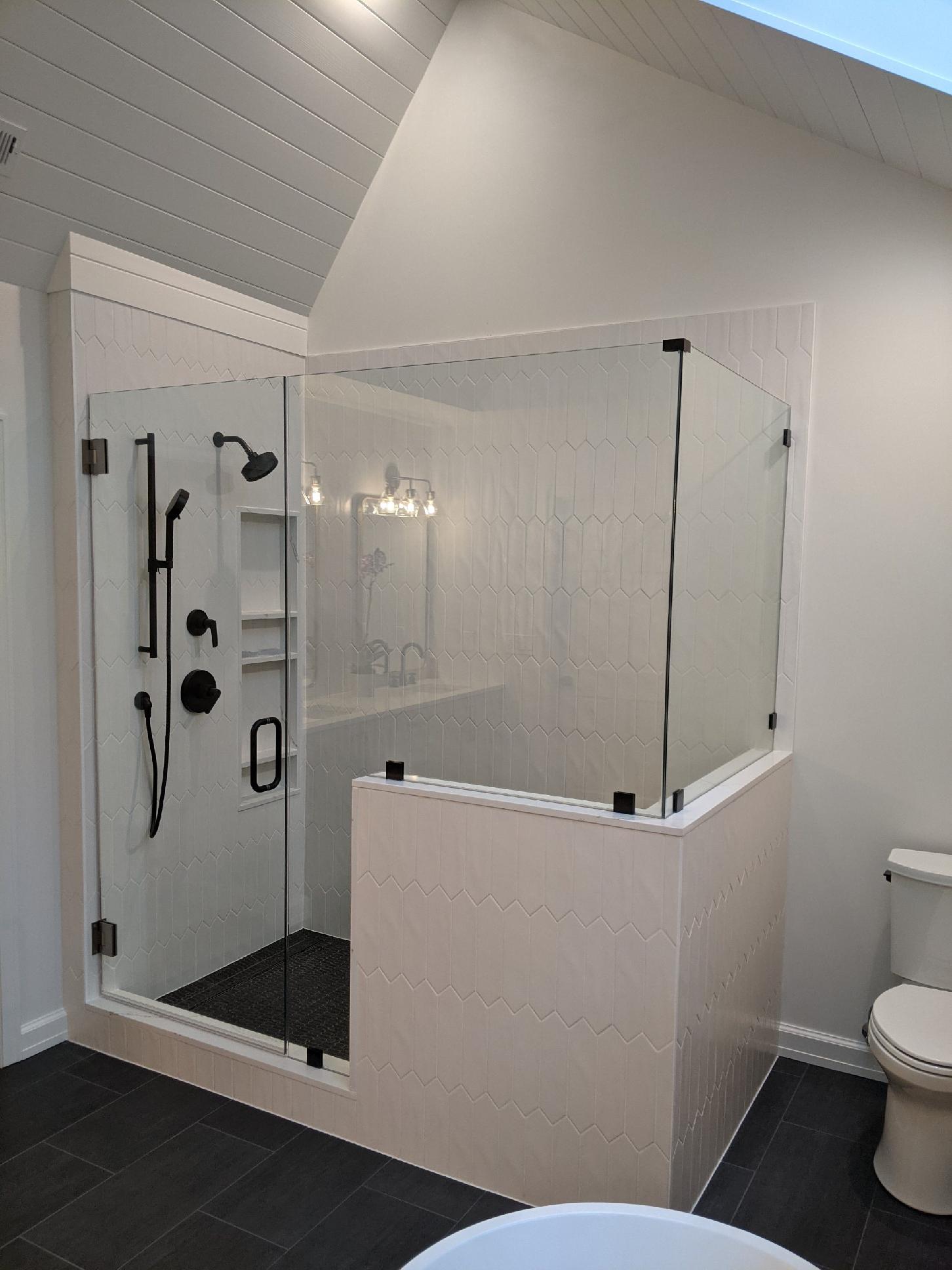 A modern walk-in shower with matte black fixtures, a glass enclosure, and a tiled half-wall in a bright bathroom.