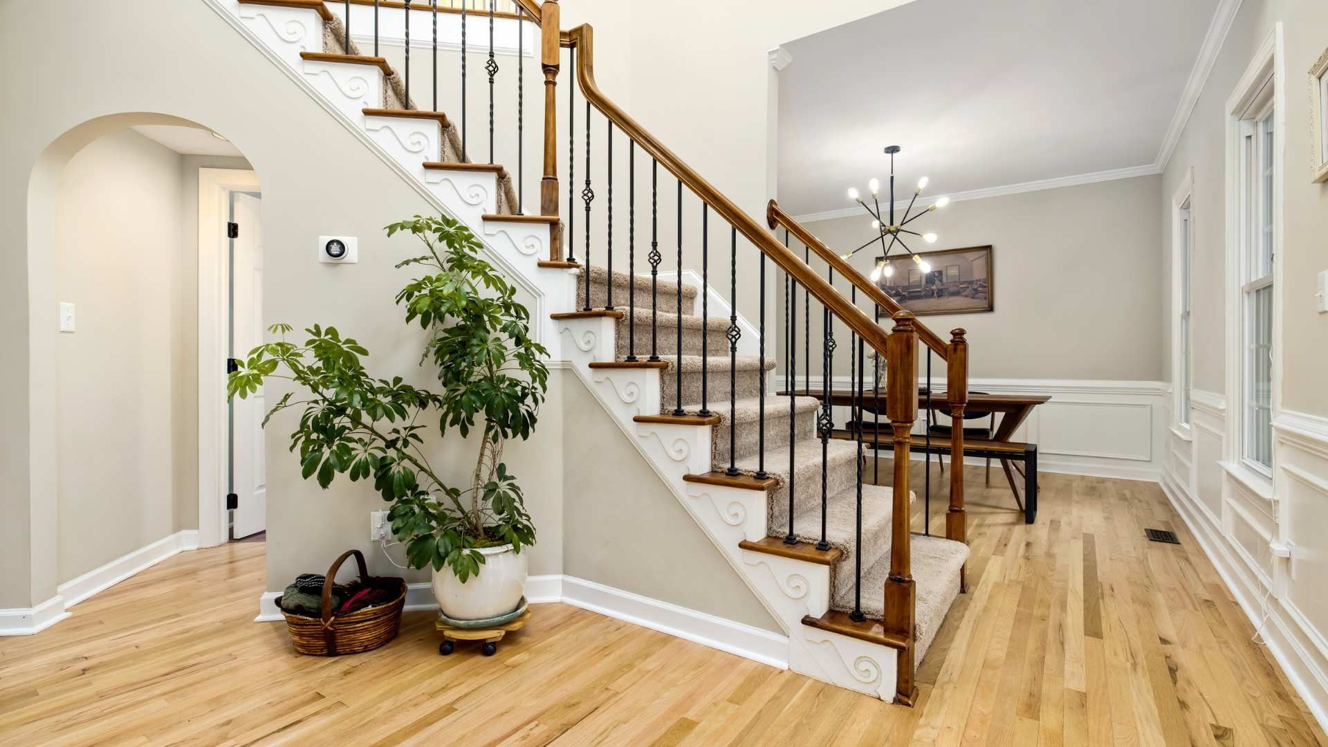 Bright foyer with hardwood floors, staircase, potted plant, and dining area in the background