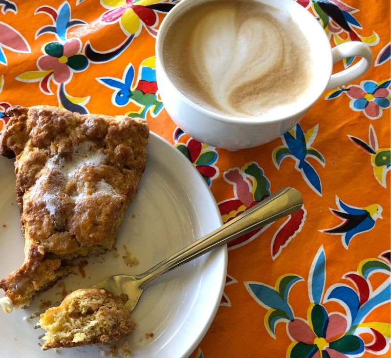 A slice of scone is on a plate next to a cup of coffee.