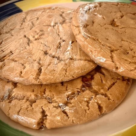 Three organic gluten free peanut butter cookies wrapped in plastic on a plate.