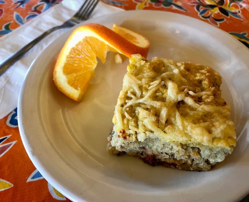 A white plate topped with a piece of savory organic scone and an orange slice.