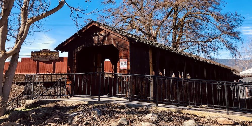 A historic covered wooden bridge is surrounded by trees and a metal fence in Yreka, CA.