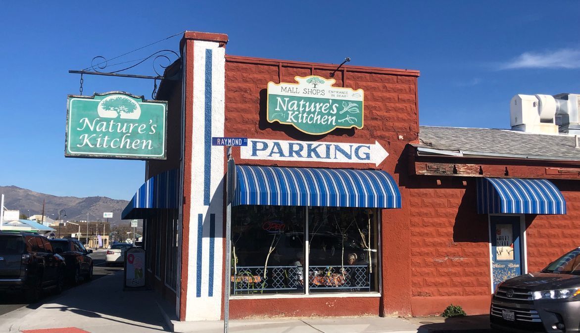 A car is parked in front of a nature 's kitchen restaurant in Yreka, CA.