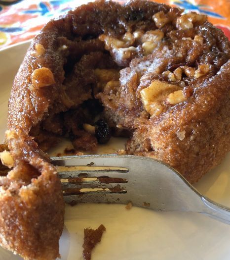 A close up of a fresh warm cinnamon roll on a plate with a fork.