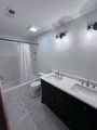 A bathroom with a black double vanity, white marble-style flooring, and a white shower-tub combination.