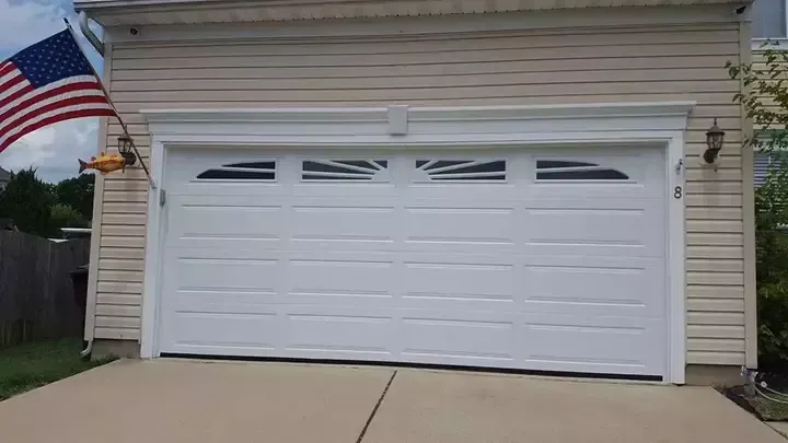 A white garage door is open in front of a house with an american flag flying in the background.