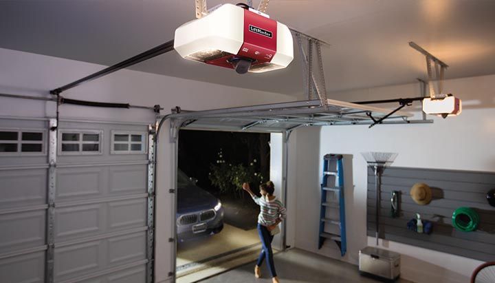 A woman is opening a garage door with a red garage door opener.