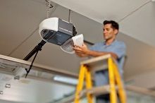 A man is standing on a ladder fixing a garage door opener.