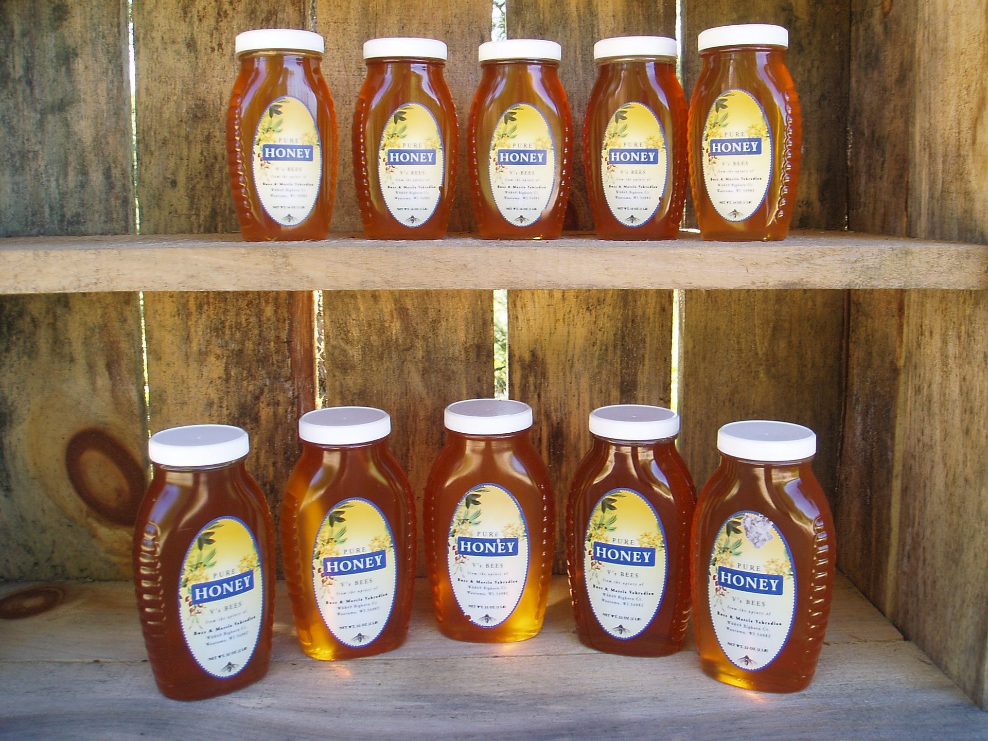 Rows of honey jars on wooden shelves, with amber liquid and white lids.