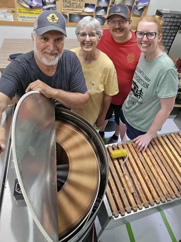 Four people stand by a large metal food mixer in a kitchen or workshop, smiling at the camera.