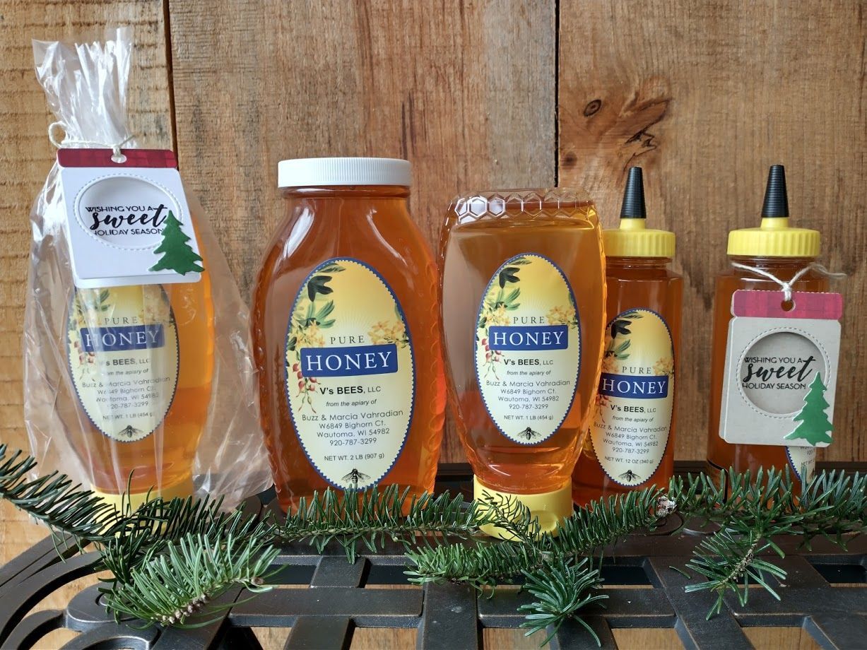 Assorted honey jars and squeezers arranged on a wooden surface with pine sprigs.