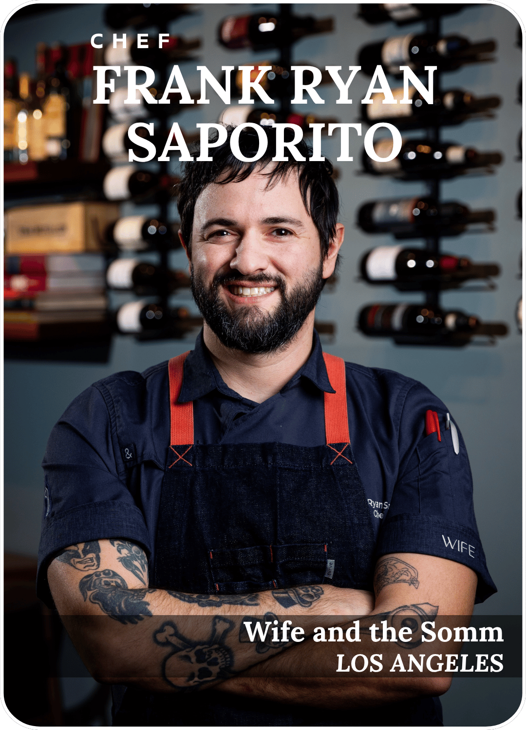 Chef Frank Ryan Saporito smiling in a navy shirt and red apron, standing before wine bottles.