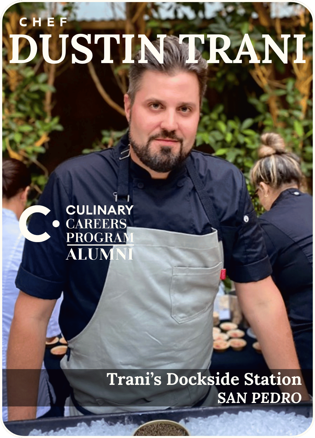 Chef Dustin Trani standing in a navy shirt and gray apron at Trani’s Dockside Station, San Pedro.