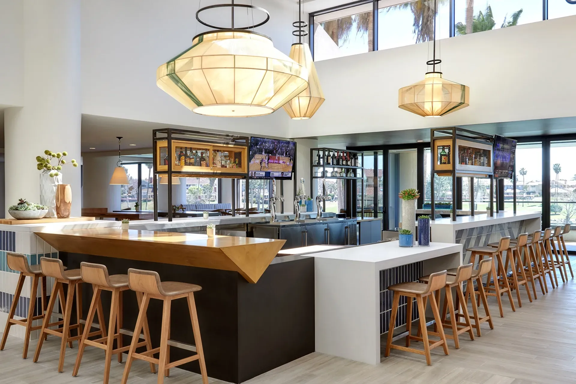 Modern bar interior with wooden stools, white countertops, and hanging geometric pendant lights