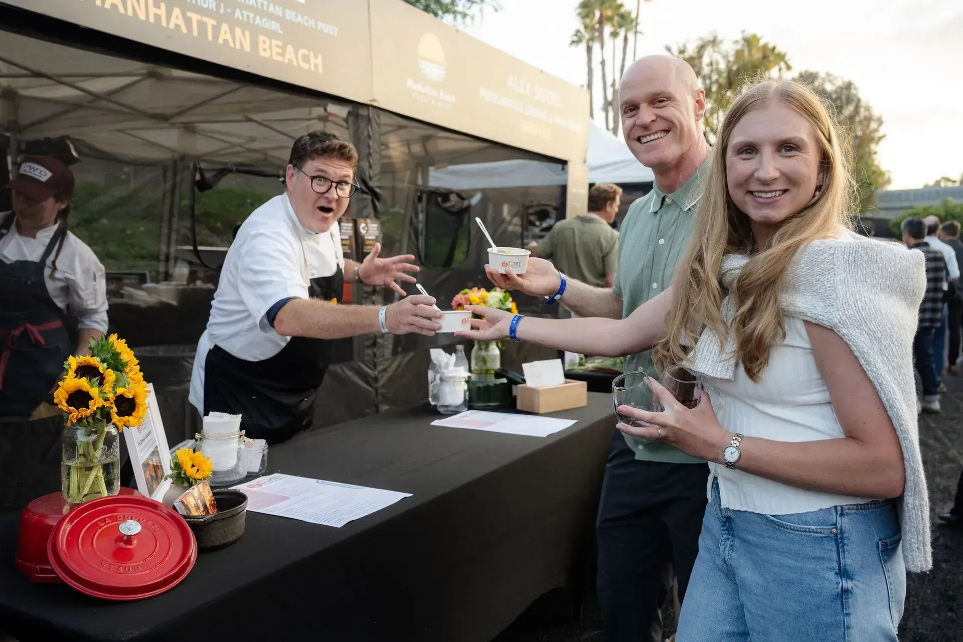 People serving drinks at an outdoor event booth with a smiling woman holding a cup