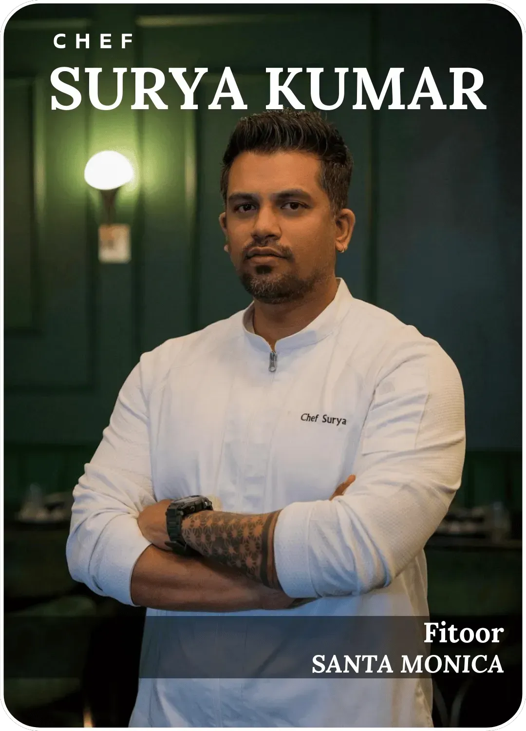 Chef Surya Kumar stands with arms crossed in a white jacket against a dark green backdrop.