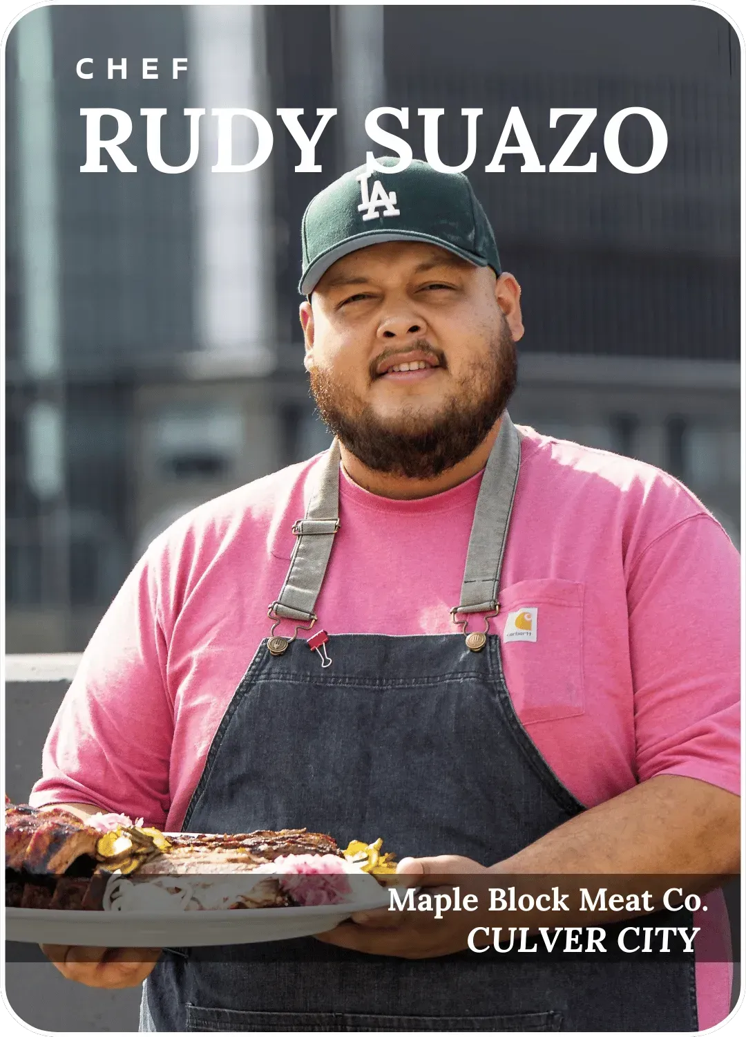 Chef Rudy Suazo holding a plated dish, wearing a pink shirt and black apron, with 