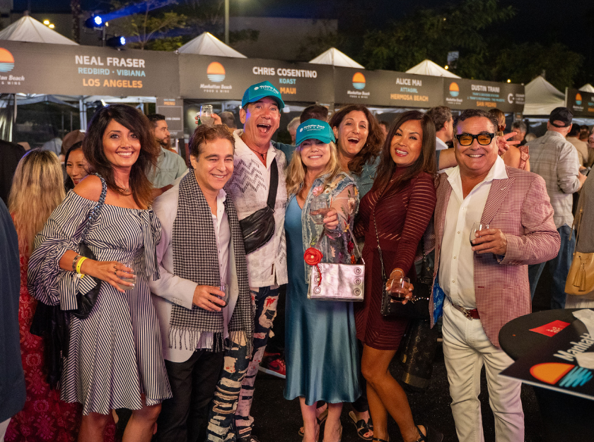 Group of smiling people posing outdoors at night in front of event tents, holding a framed item.