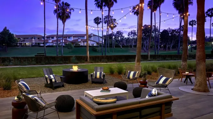Outdoor patio lounge with string lights, fire pit, and cushioned seating at dusk